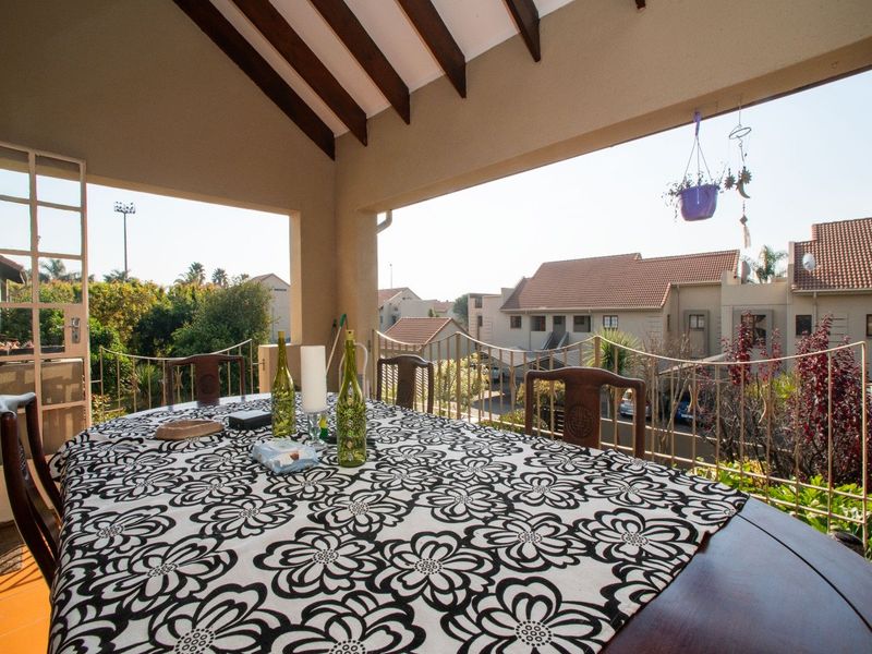 A covered balcony featuring exposed timber rafters, tiled flooring, and a metal balustrade, offering an open-air space with views of the surrounding townhouse complex.