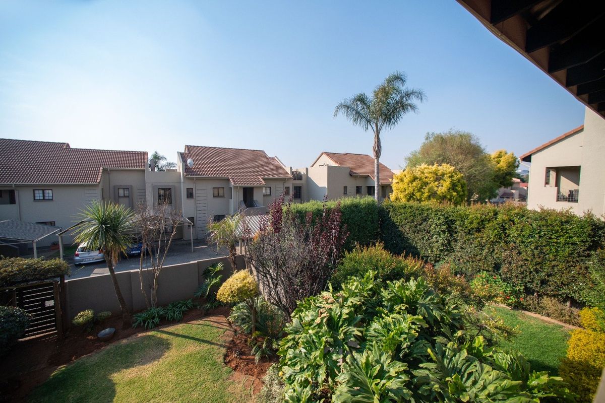 Elevated view of a well-maintained townhouse complex featuring a landscaped garden, paved driveway, and covered carport area.
