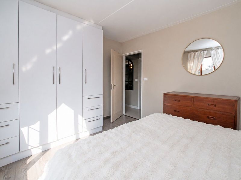 A well-maintained bedroom featuring modern white built-in cupboards, neutral wall tones, and durable laminate flooring, offering a clean and functional living space.