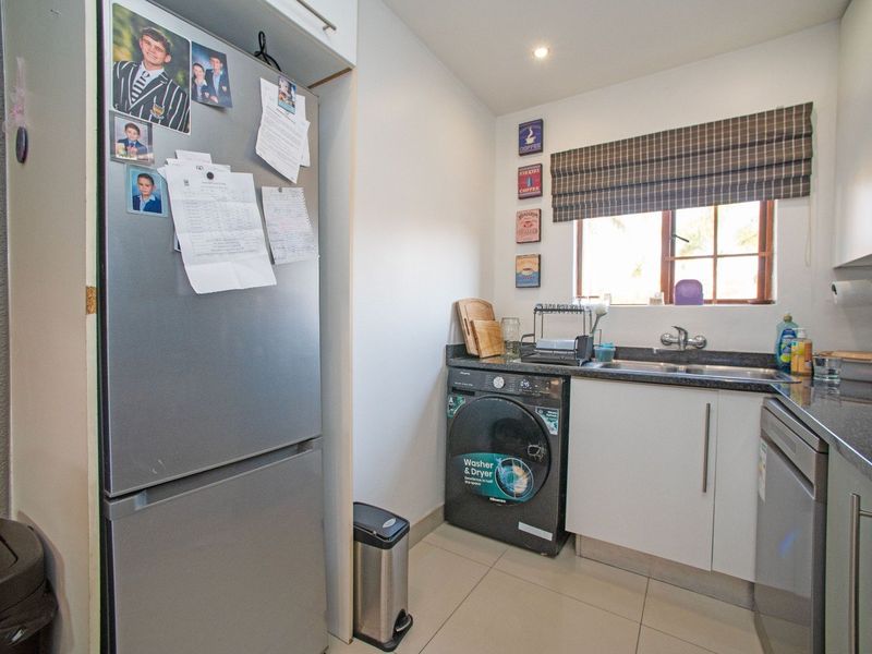 Compact scullery featuring granite countertops, stainless steel sink, and built-in cabinetry, providing efficient workspace and laundry utility.