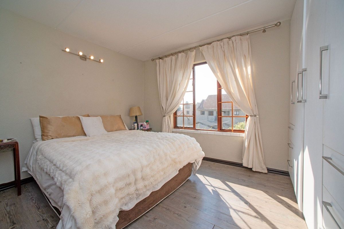 A bright bedroom featuring laminate flooring, a built-in wardrobe, and a timber-framed window allowing for natural light.