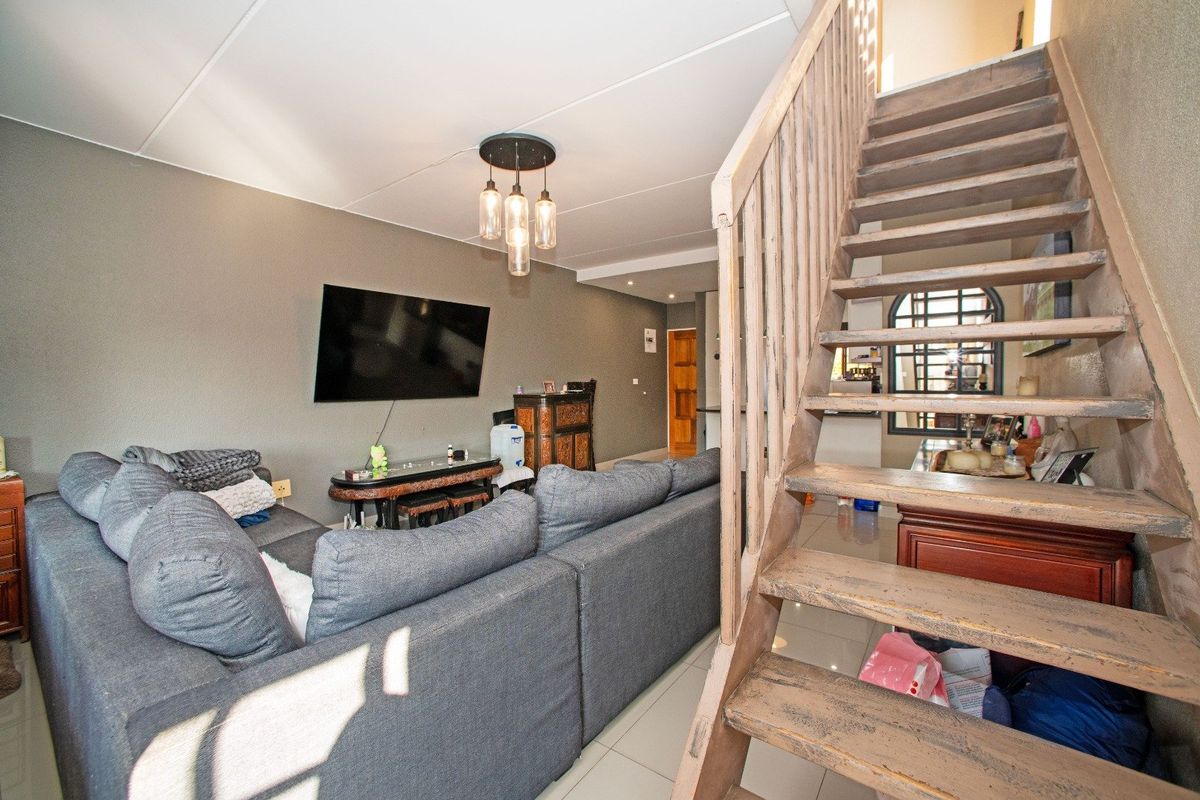 Open-plan living area featuring a wooden staircase, tiled flooring, and modern pendant lighting, providing a functional space for relaxation and access to upper levels.