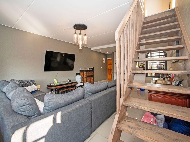 Open-plan living area featuring a wooden staircase, tiled flooring, and modern pendant lighting, providing a functional space for relaxation and access to upper levels.