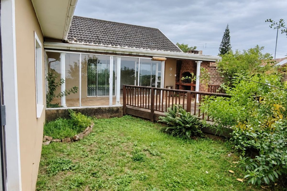 Rear exterior view featuring a wooden deck, built-in brick braai, and an enclosed patio area with sliding glass doors.