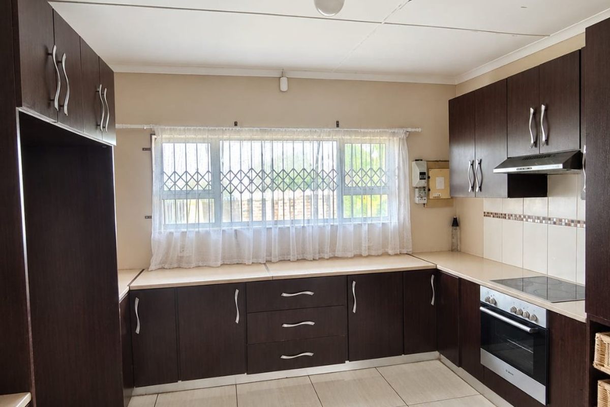 A functional kitchen featuring dark wood cabinetry, built-in oven, electric hob, extractor fan, and tiled flooring, offering a clean and practical workspace.
