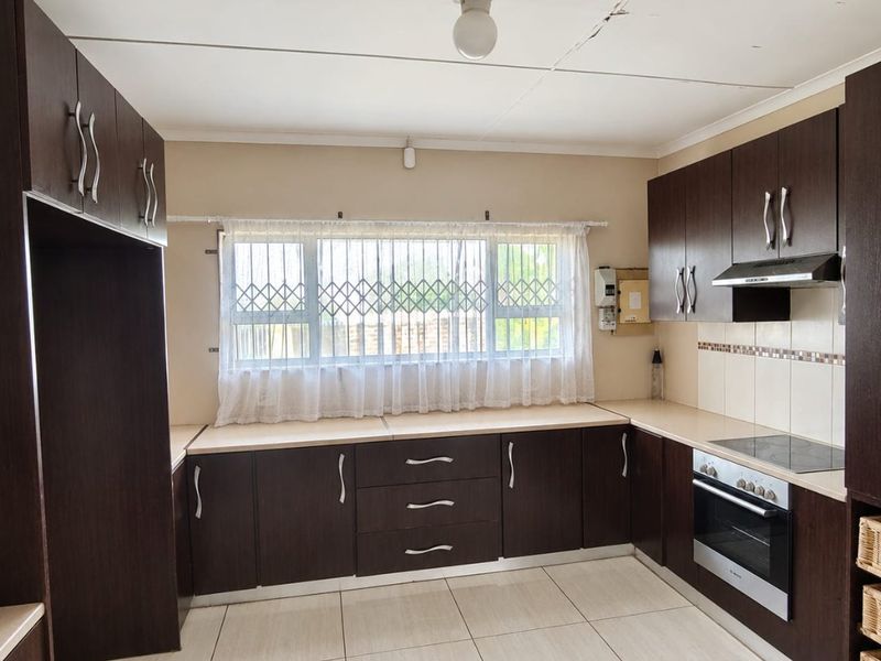 A functional kitchen featuring dark wood cabinetry, built-in oven, electric hob, extractor fan, and tiled flooring, offering a clean and practical workspace.