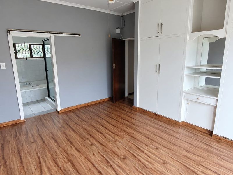 Spacious bedroom featuring laminate flooring, built-in cupboards with vanity area, ceiling fan, and direct access to an en-suite bathroom.