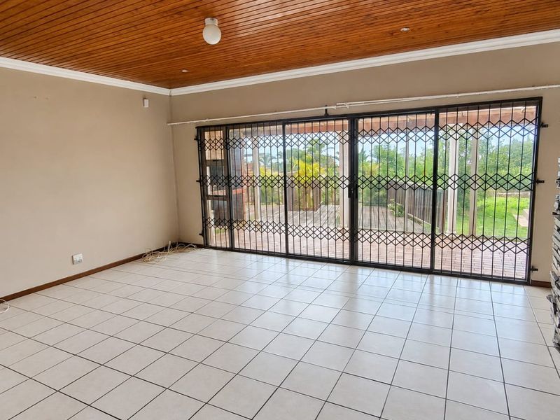 Spacious living area featuring tiled floors, a warm wooden ceiling, and large sliding doors with security gates opening to an outdoor patio.