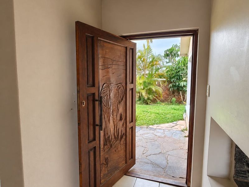 An entrance area featuring a decorative carved wooden door, tiled flooring, and a built-in wall niche, leading out to a garden patio.
