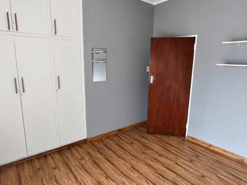 A clean, empty bedroom featuring modern laminate flooring, built-in white cupboards, and neutral grey walls, ready for personalization.