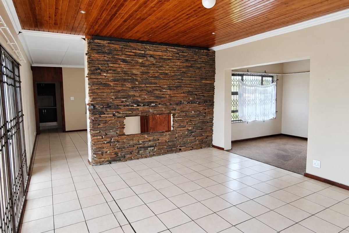 Spacious living area featuring a prominent stone fireplace, timber ceiling, and neutral ceramic floor tiles, offering a versatile layout for modern updates.