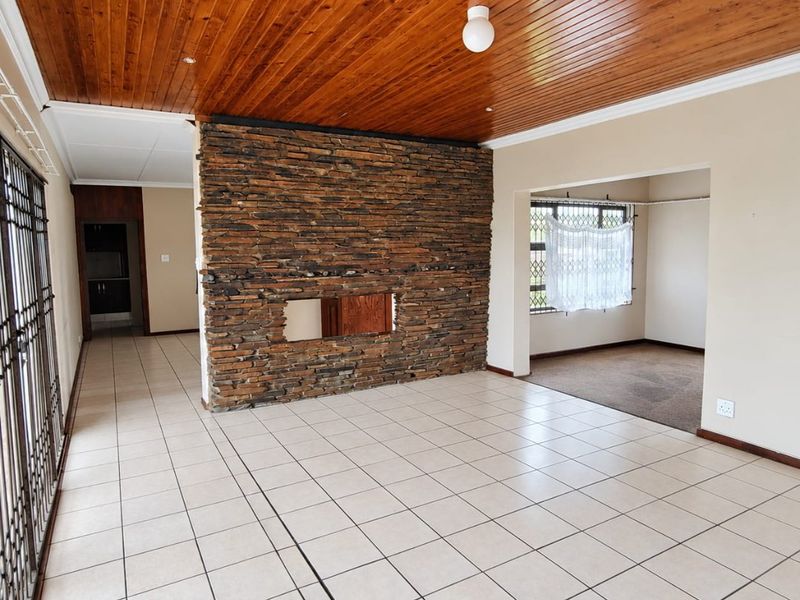 Spacious living area featuring a prominent stone fireplace, timber ceiling, and neutral ceramic floor tiles, offering a versatile layout for modern updates.