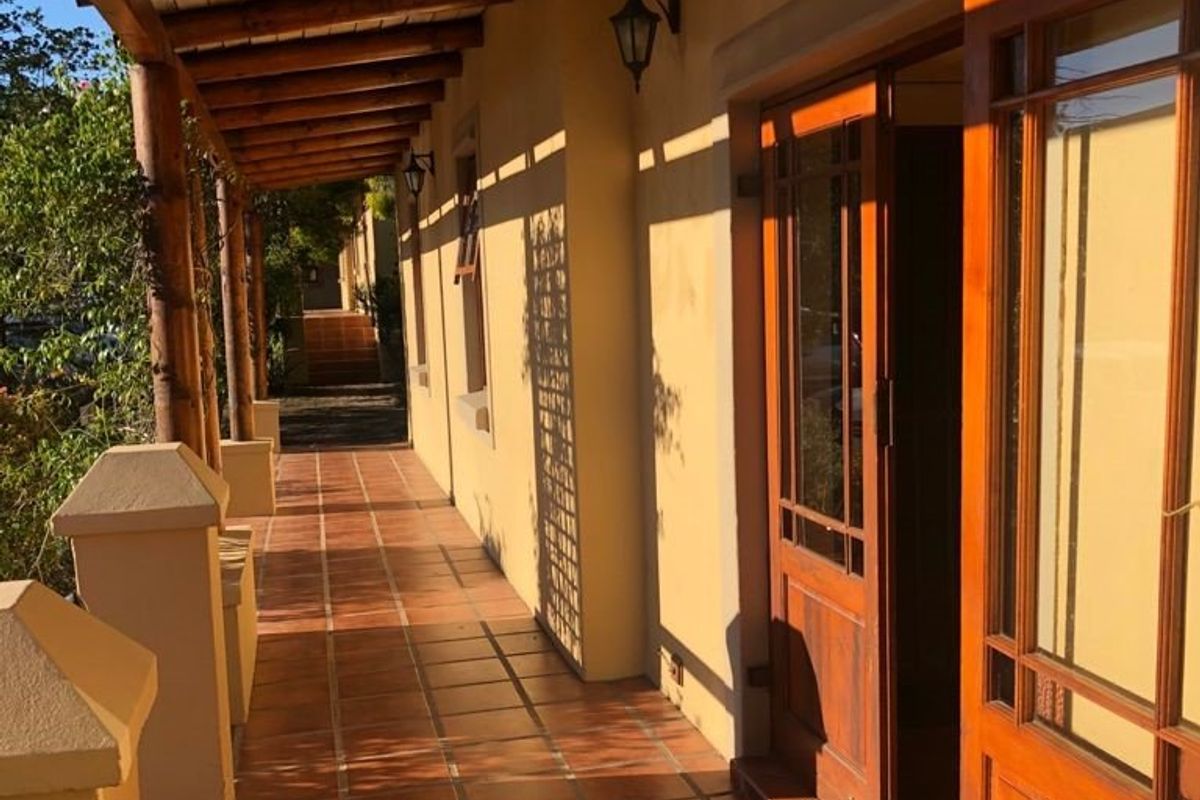 A covered outdoor patio featuring terracotta tile flooring, a timber pergola structure, and timber-framed glass doors leading into the building.
