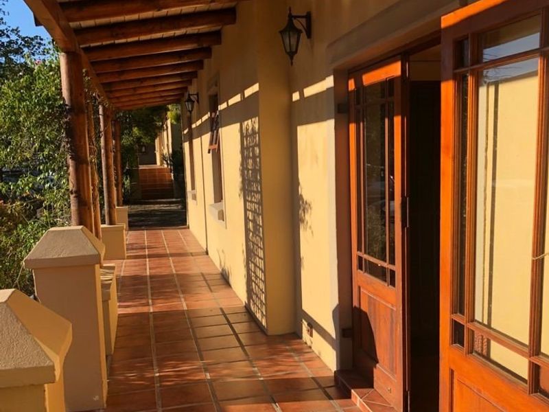 A covered outdoor patio featuring terracotta tile flooring, a timber pergola structure, and timber-framed glass doors leading into the building.