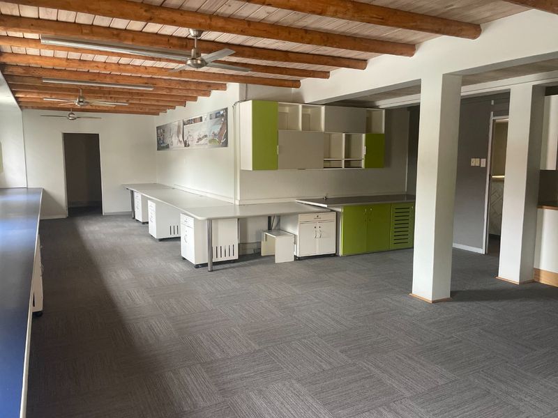 Spacious commercial office area featuring exposed timber beam ceilings, ceiling fans, fitted desks, and built-in cabinetry with a neutral carpet finish.