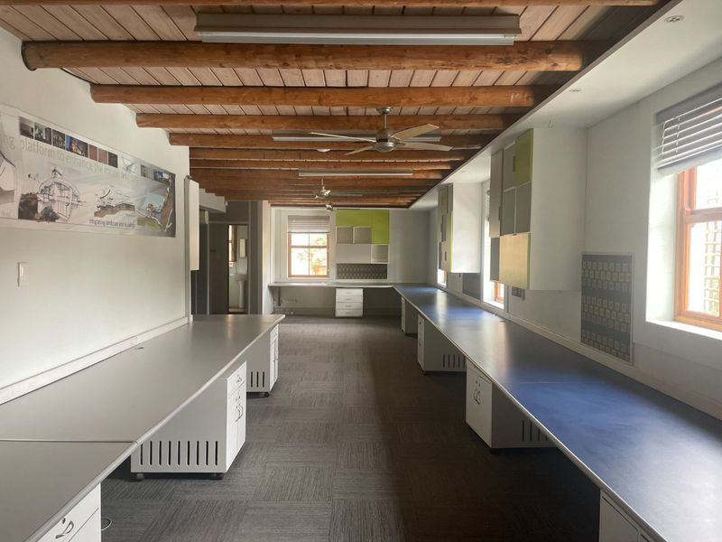 Spacious commercial office area featuring exposed timber beam ceilings, extensive built-in desk workstations, ample cabinetry, and large windows providing natural light.