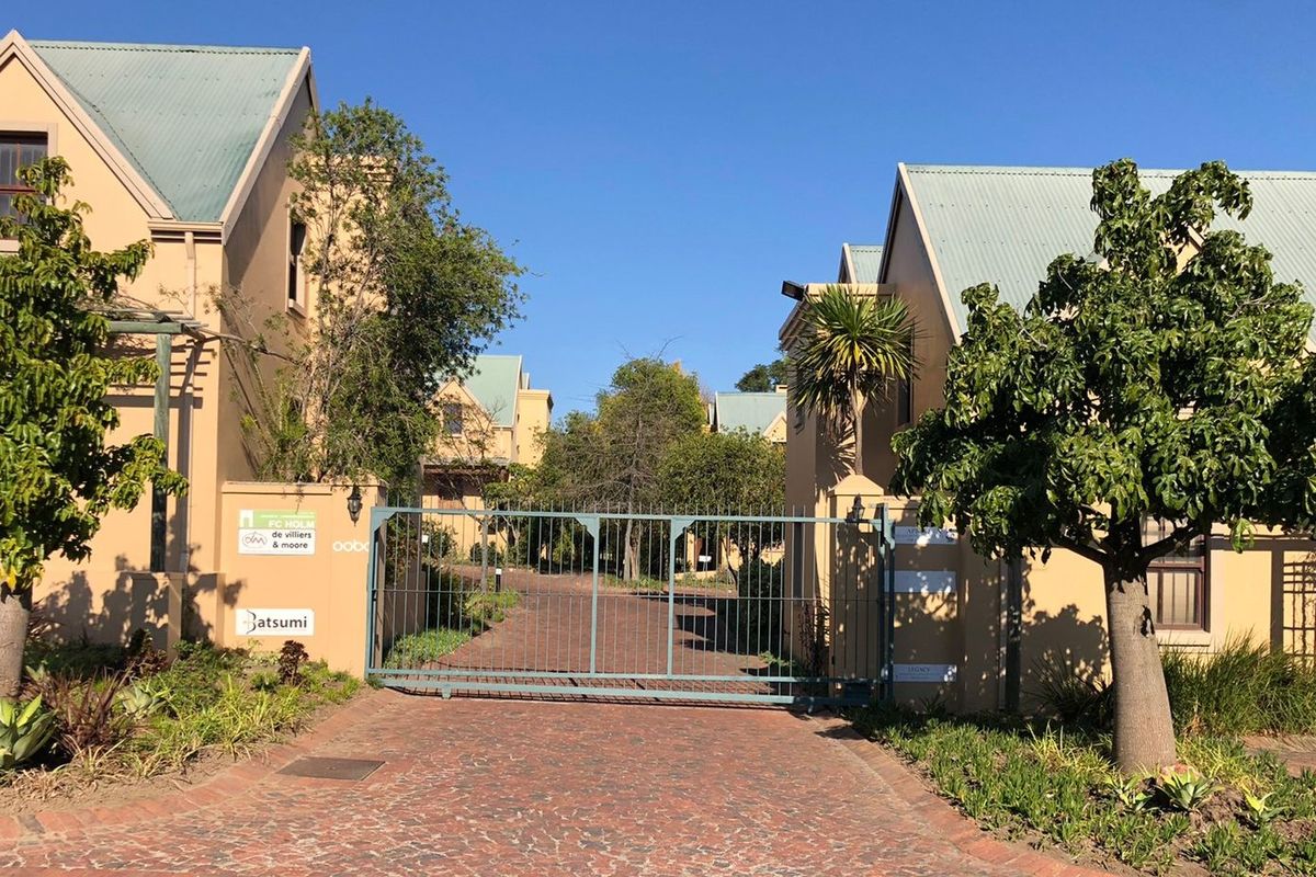Front entrance view of a commercial property complex featuring a secure metal gate, brick paved driveway, and well-maintained stucco buildings with pitched roofs.