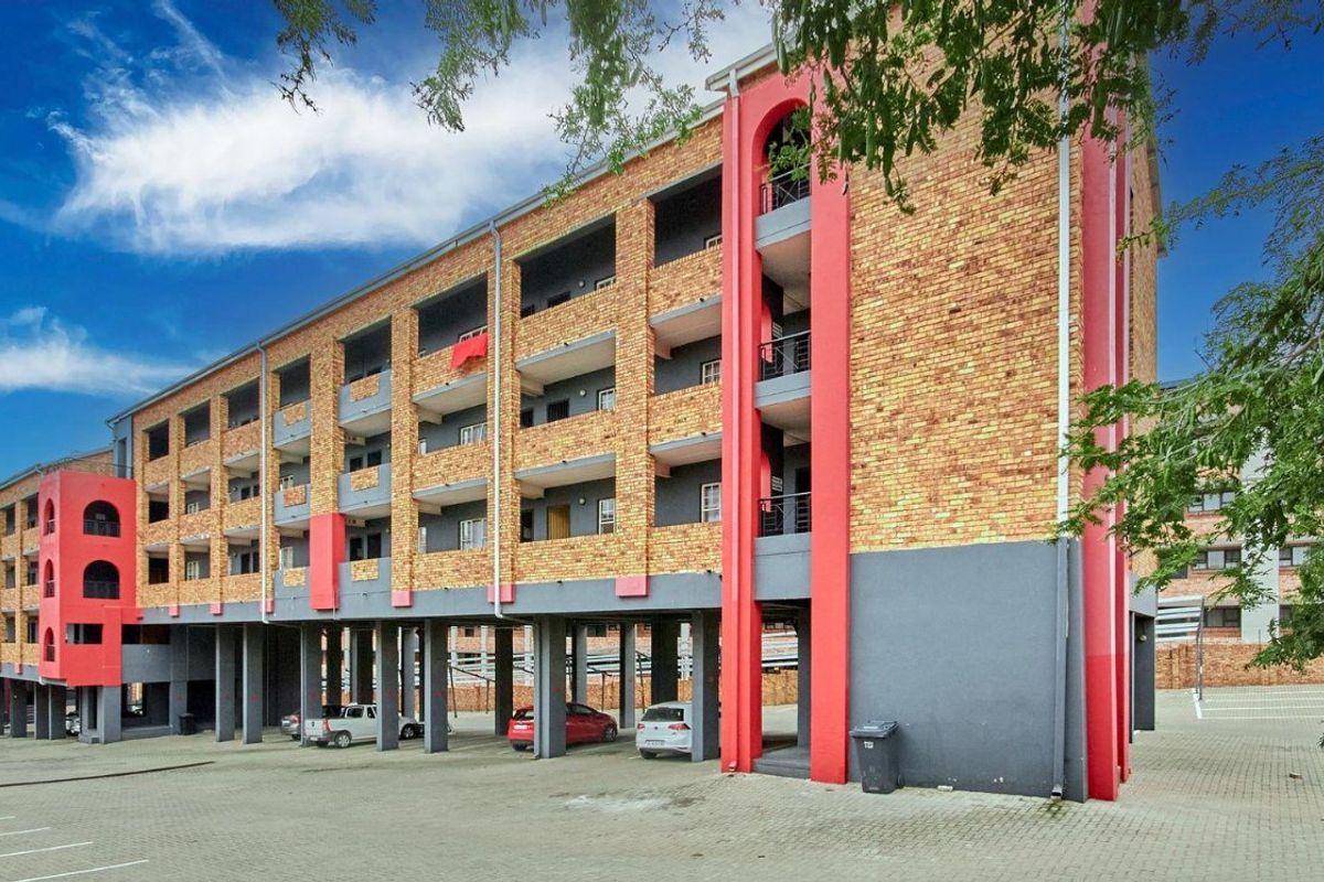 Exterior view of a multi-story apartment building featuring face brick facade, covered balconies, and ground-level stilt parking.