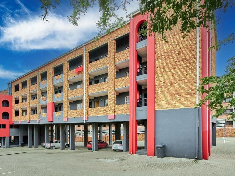 Exterior view of a multi-story apartment building featuring face brick facade, covered balconies, and ground-level stilt parking.