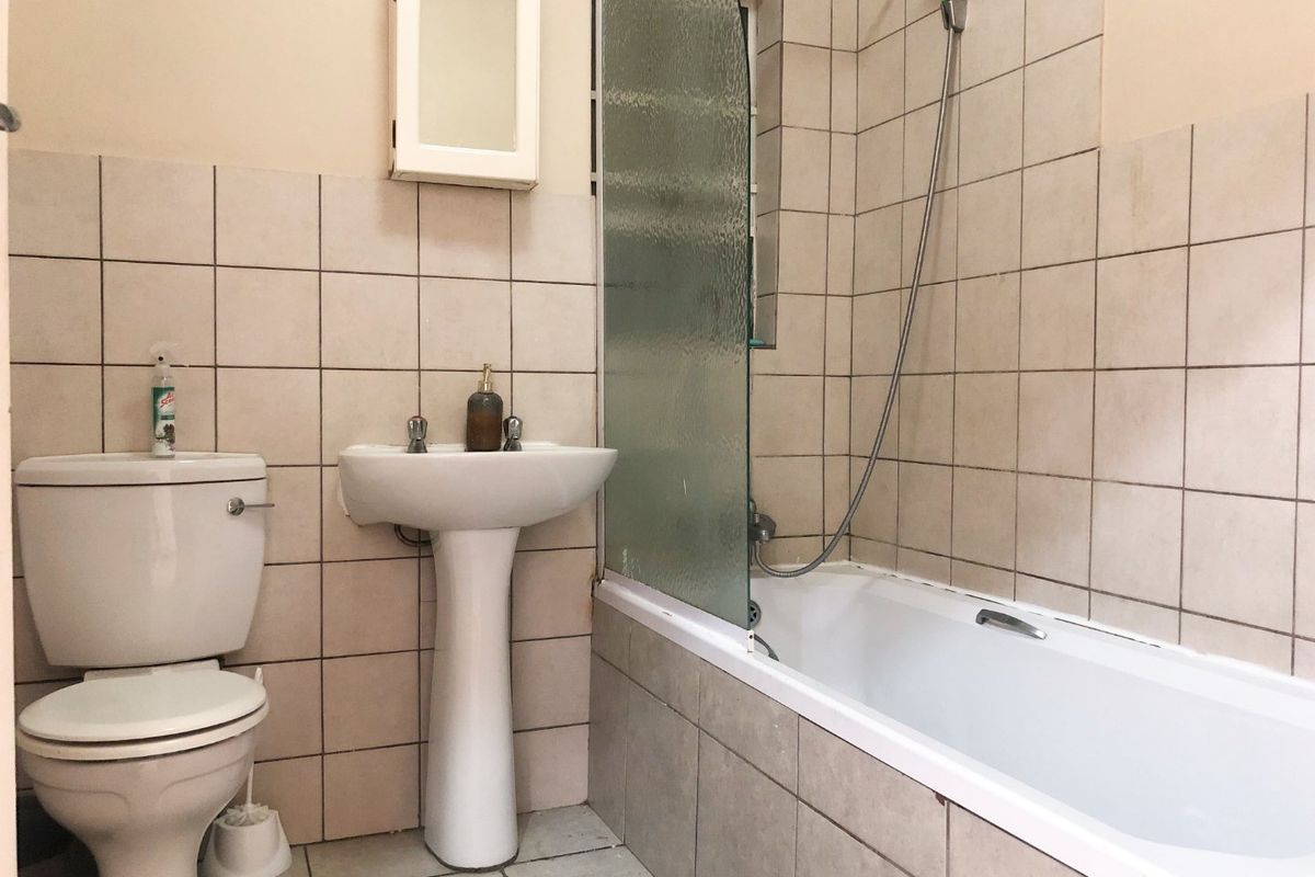 A functional bathroom featuring a pedestal basin, toilet, and a bathtub with a glass shower screen, finished with neutral ceramic wall and floor tiles.