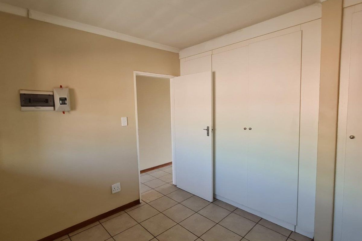 An empty bedroom featuring tiled flooring, built-in cupboards, and a wall-mounted electrical distribution board.