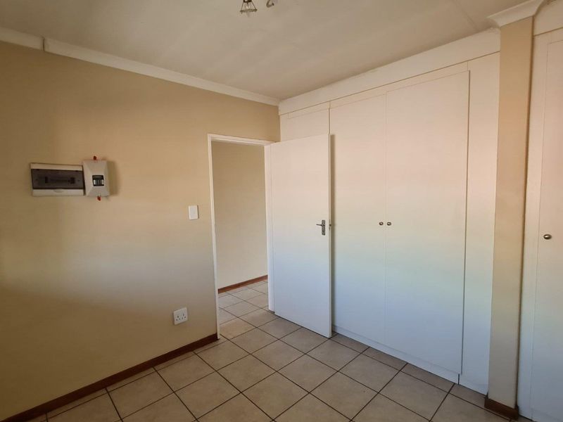 An empty bedroom featuring tiled flooring, built-in cupboards, and a wall-mounted electrical distribution board.
