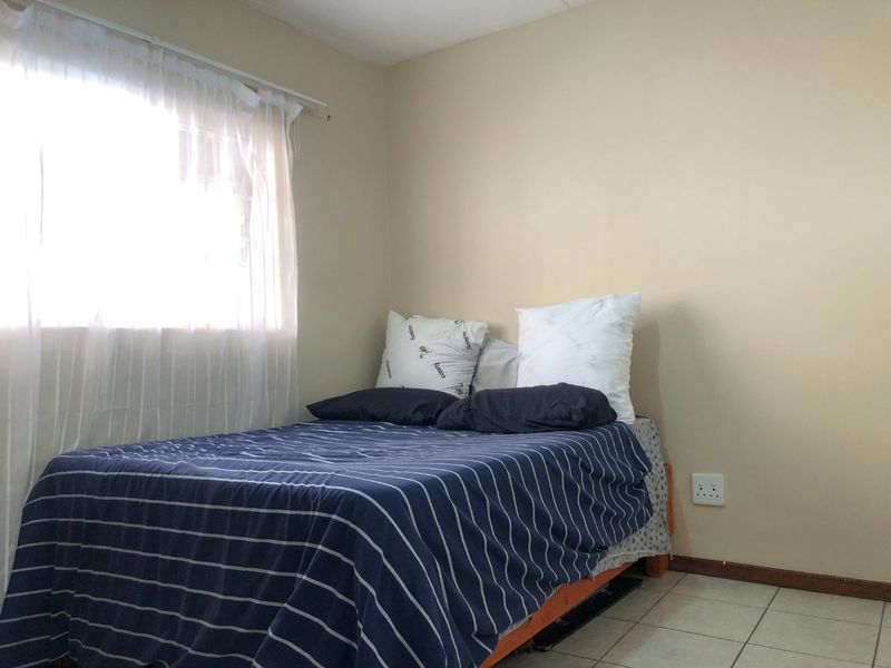 A simple bedroom featuring tiled flooring, neutral wall paint, and a window with a curtain rod.