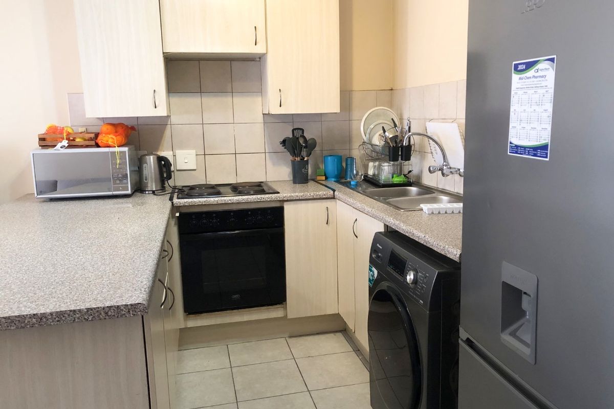 Compact kitchen featuring light-toned cabinetry, laminate countertops, built-in oven and hob, tiled backsplash, and integrated space for laundry appliances.