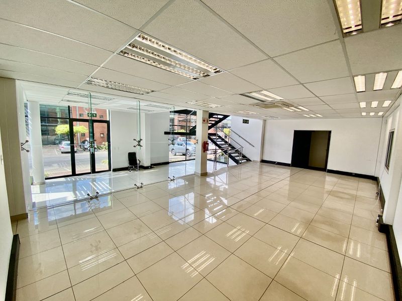 Spacious open-plan industrial office area featuring tiled flooring, suspended ceilings with integrated lighting, glass partitioning, and a modern metal staircase.