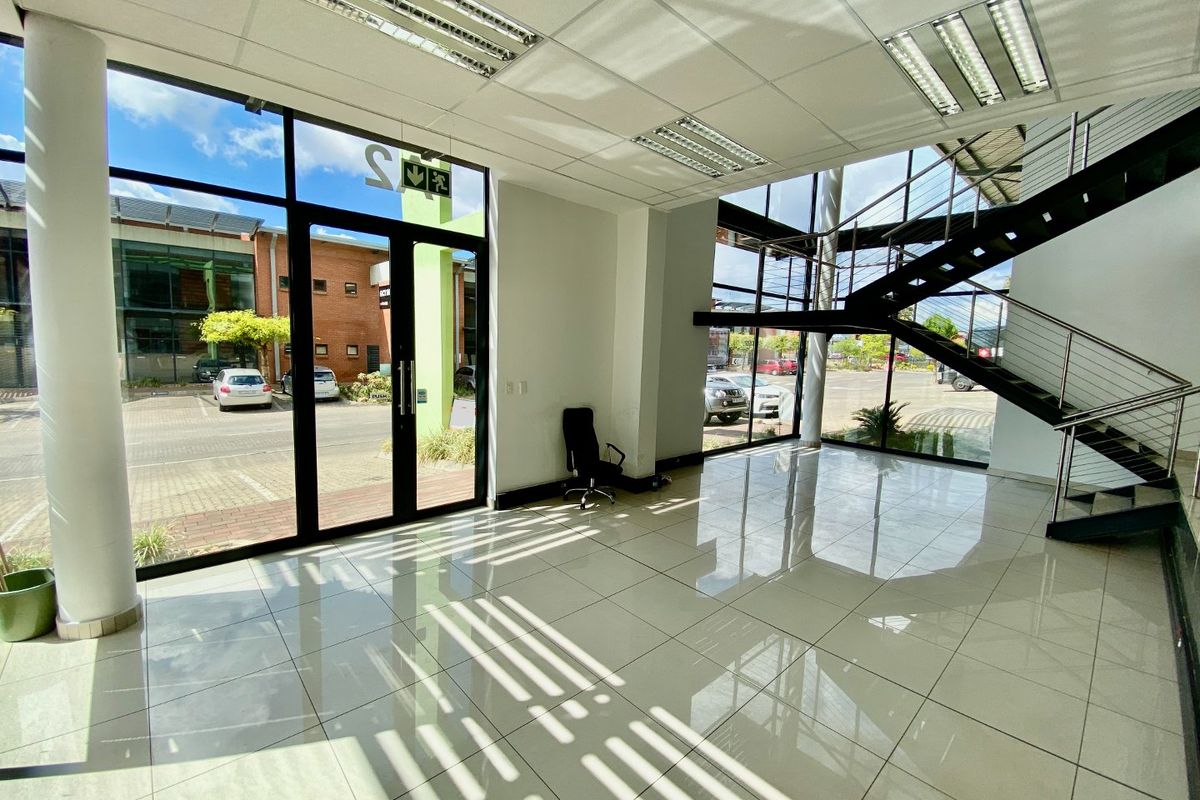 Spacious industrial entrance lobby featuring high ceilings, large glass windows, polished tile flooring, and a modern metal staircase.