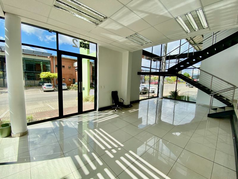 Spacious industrial entrance lobby featuring high ceilings, large glass windows, polished tile flooring, and a modern metal staircase.