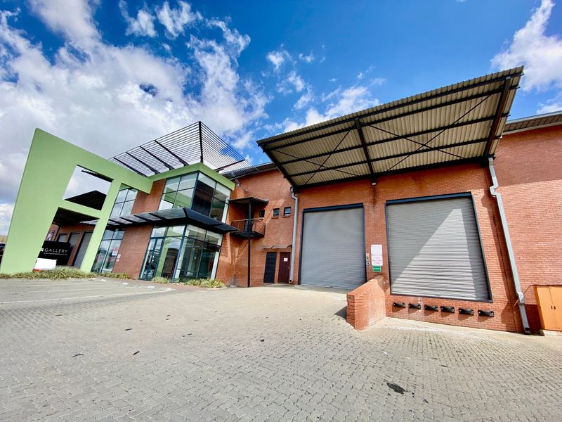 Front elevation of an industrial property featuring a loading bay with roller shutter doors, brick facade, and modern glass office entrance.