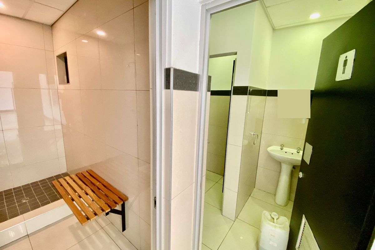 A clean, functional industrial bathroom facility featuring tiled surfaces, a pedestal sink, and a shower cubicle with a built-in wooden bench.
