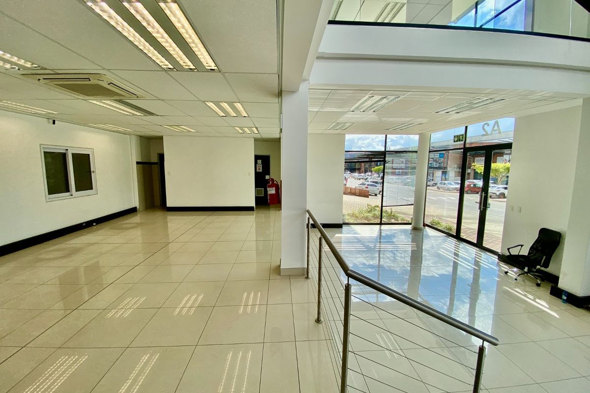Spacious open-plan industrial office area featuring polished tile flooring, recessed lighting, and large glass windows providing ample natural light and street visibility.