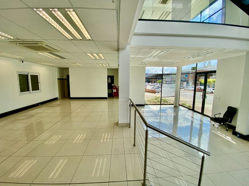 Spacious open-plan industrial office area featuring polished tile flooring, recessed lighting, and large glass windows providing ample natural light and street visibility.
