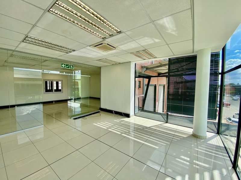 Modern open-plan office space featuring polished tile flooring, glass partitioning, suspended ceilings with recessed lighting, and large windows providing ample natural light.