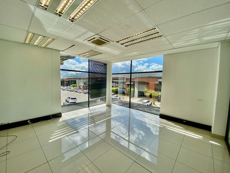A bright, vacant office space featuring large floor-to-ceiling windows, ceramic tile flooring, and a suspended ceiling with recessed lighting.