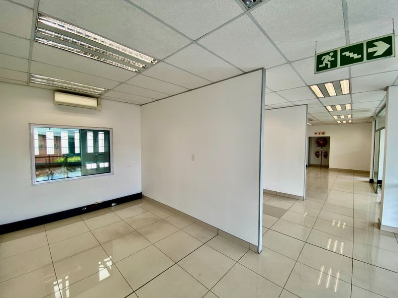 Open-plan industrial office space featuring tiled flooring, partition walls, suspended ceilings with integrated lighting, and a wall-mounted air conditioning unit.