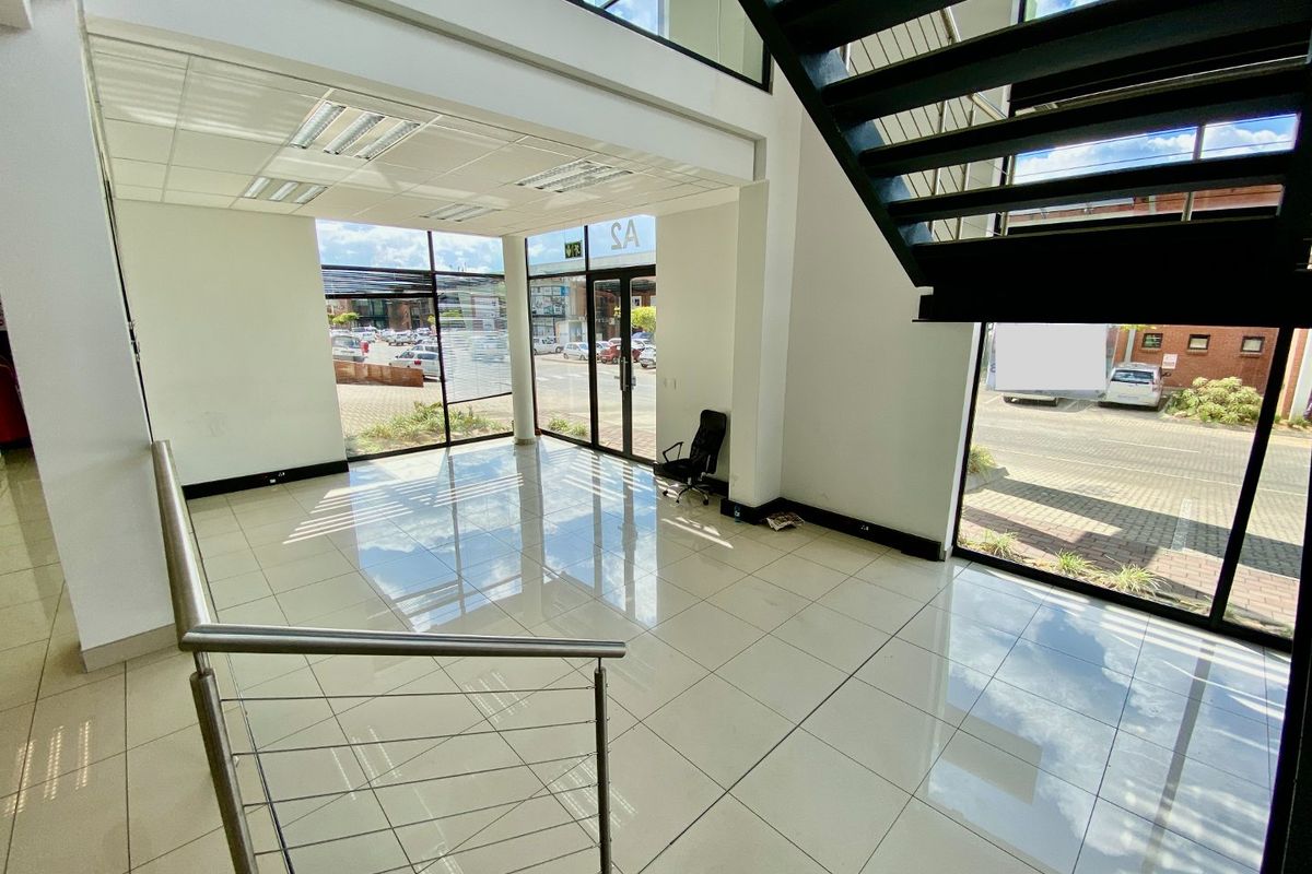 Spacious double-volume industrial entrance foyer featuring polished tiled flooring, a modern metal staircase with stainless steel balustrades, and extensive glass storefront windows.
