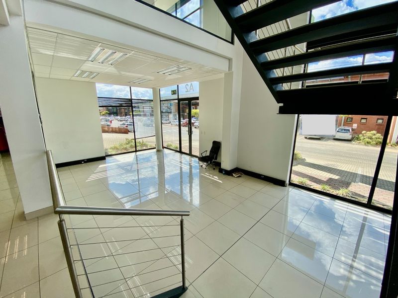 Spacious double-volume industrial entrance foyer featuring polished tiled flooring, a modern metal staircase with stainless steel balustrades, and extensive glass storefront windows.