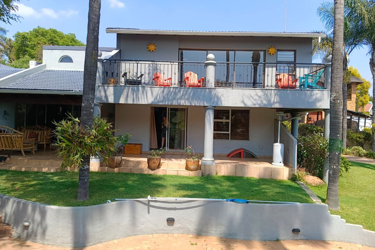 Rear view of a two-story house featuring a spacious upper balcony with wrought iron railings, a ground-level tiled patio, and a swimming pool.