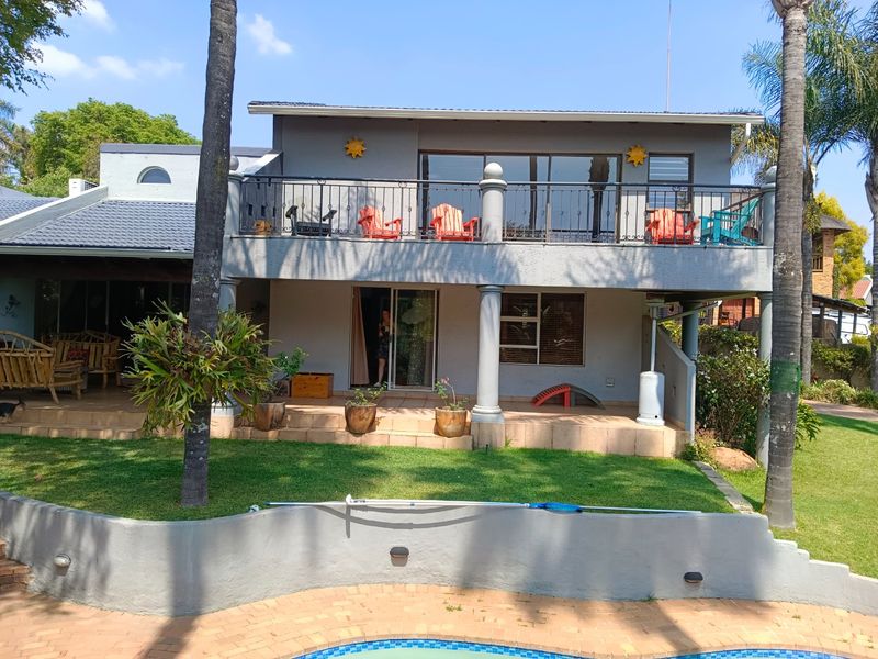 Rear view of a two-story house featuring a spacious upper balcony with wrought iron railings, a ground-level tiled patio, and a swimming pool.