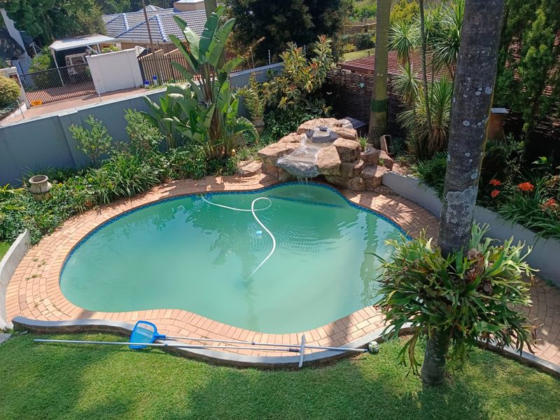 A backyard swimming pool featuring a rock water feature, brick coping, and surrounding landscaped garden area.