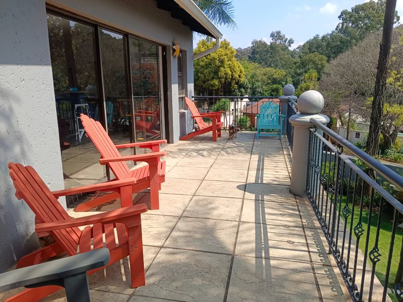 Spacious elevated balcony featuring tiled flooring and a decorative wrought iron balustrade, offering a pleasant outdoor seating area with garden views.