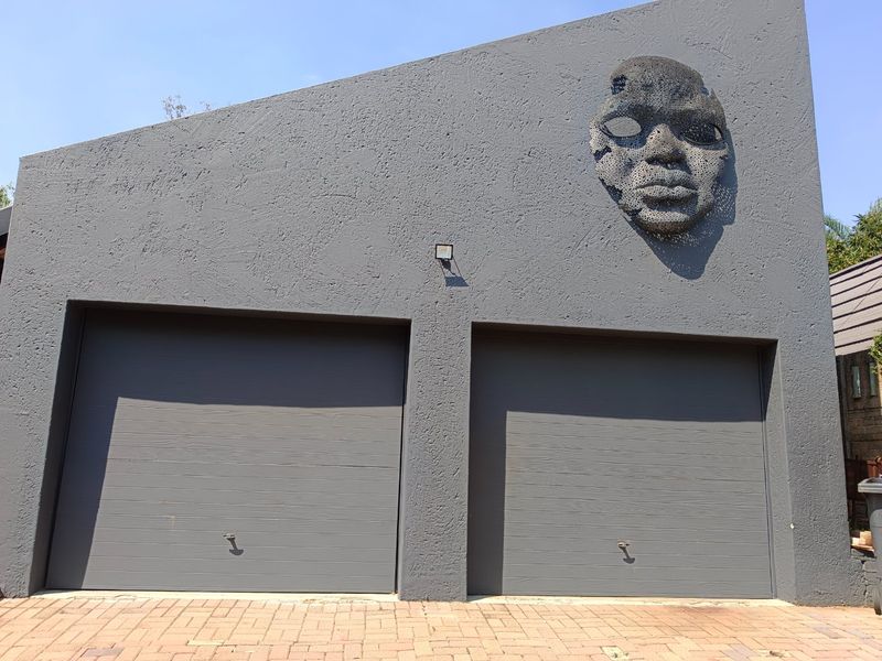 A modern double garage facade featuring a textured grey finish and a unique decorative wall sculpture above the garage doors.
