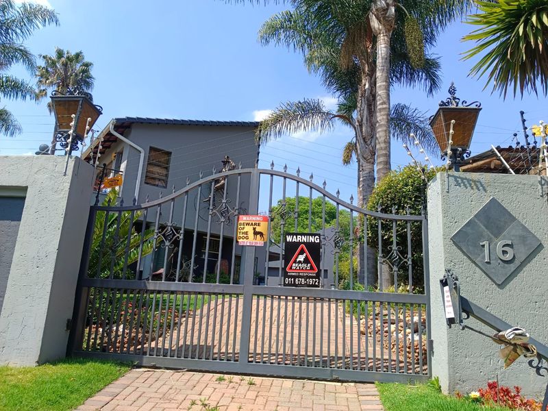 Front entrance view featuring a secure wrought iron gate, brick driveway, and perimeter electric fencing with mounted pillar lanterns.