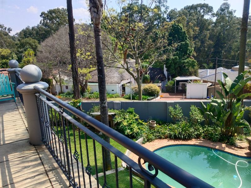 Elevated balcony overlooking a private garden with a swimming pool, featuring a wrought iron balustrade and views of the surrounding neighborhood.