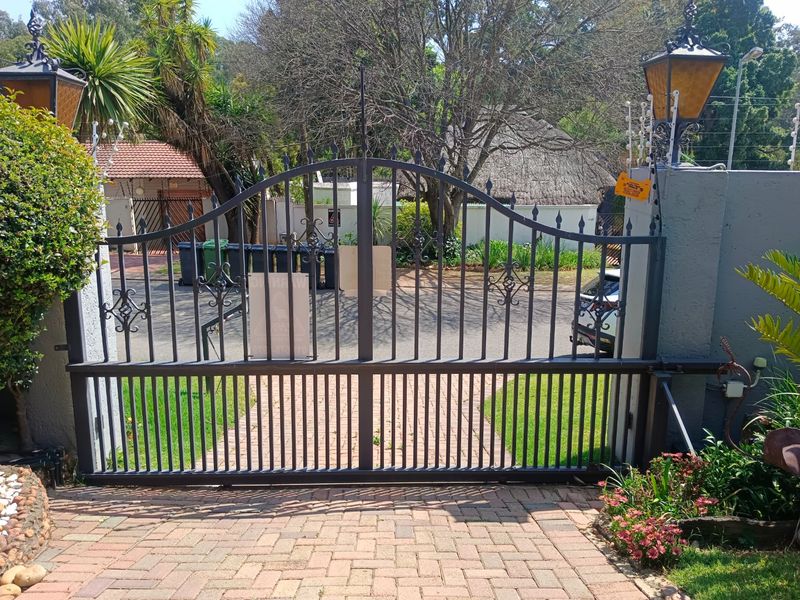 A secure front entrance featuring a wrought iron gate, brick paved driveway, and perimeter electric fencing.
