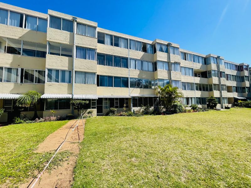 Rear view of a multi-story apartment building featuring a large communal lawn and brick facade with extensive window glazing.