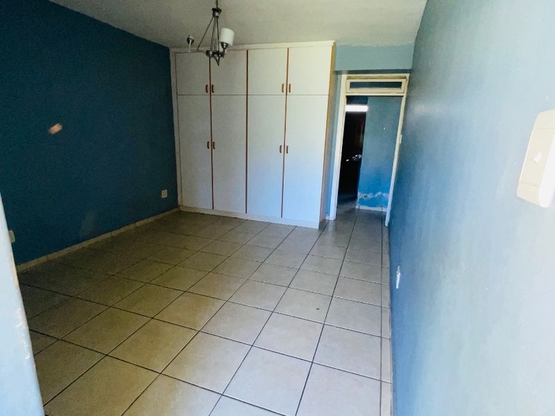 An empty bedroom featuring tiled flooring and built-in cupboards, requiring minor cosmetic updates to the wall finishes.
